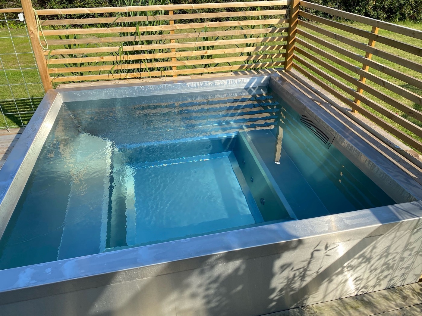 Stainless steel pool built into a deck with a privacy screen